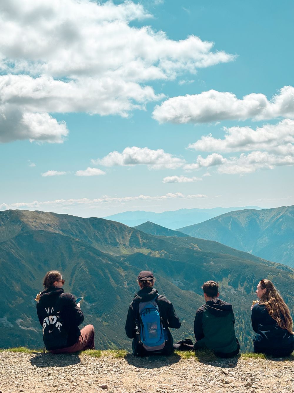 Fire unge sitter i en fjellside og ser utover fjell og skyer